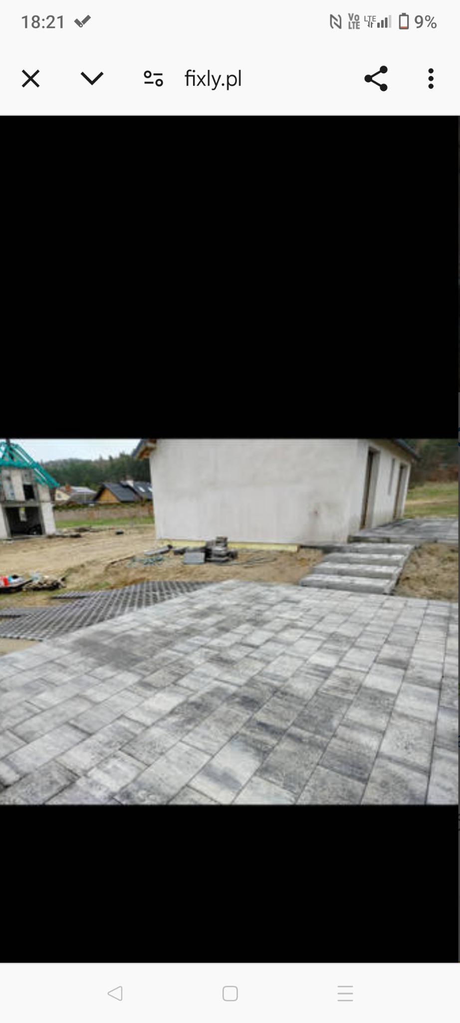 Ułożona szara kostka brukowa przed budynkiem gospodarczym z schodami, widoczny fundament domu w budowie w tle.