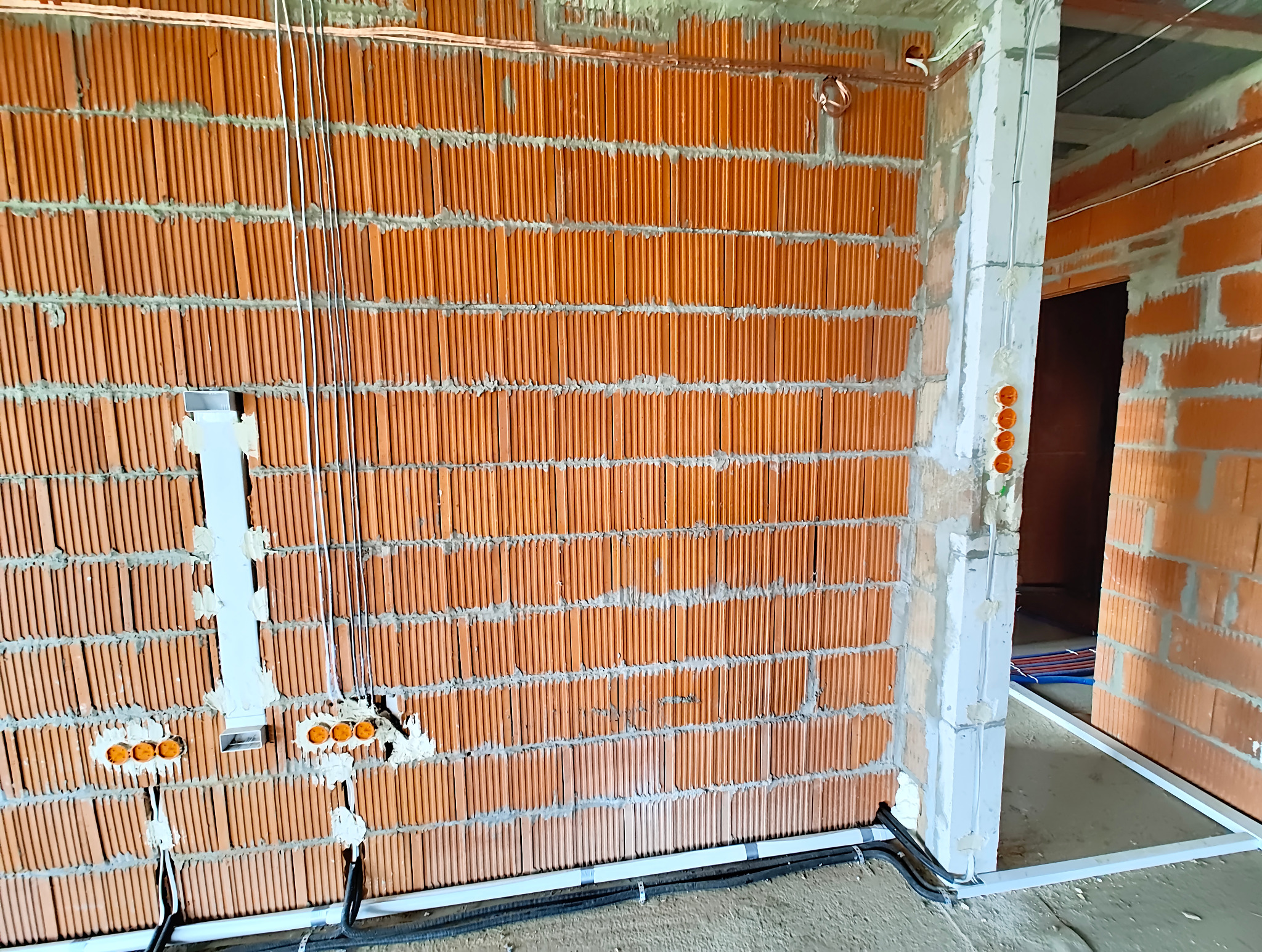 Wewnętrzna instalacja elektryczna w surowym domu jednorodzinnym z cegły, widoczne kable, puszki instalacyjne i rury ochronne.