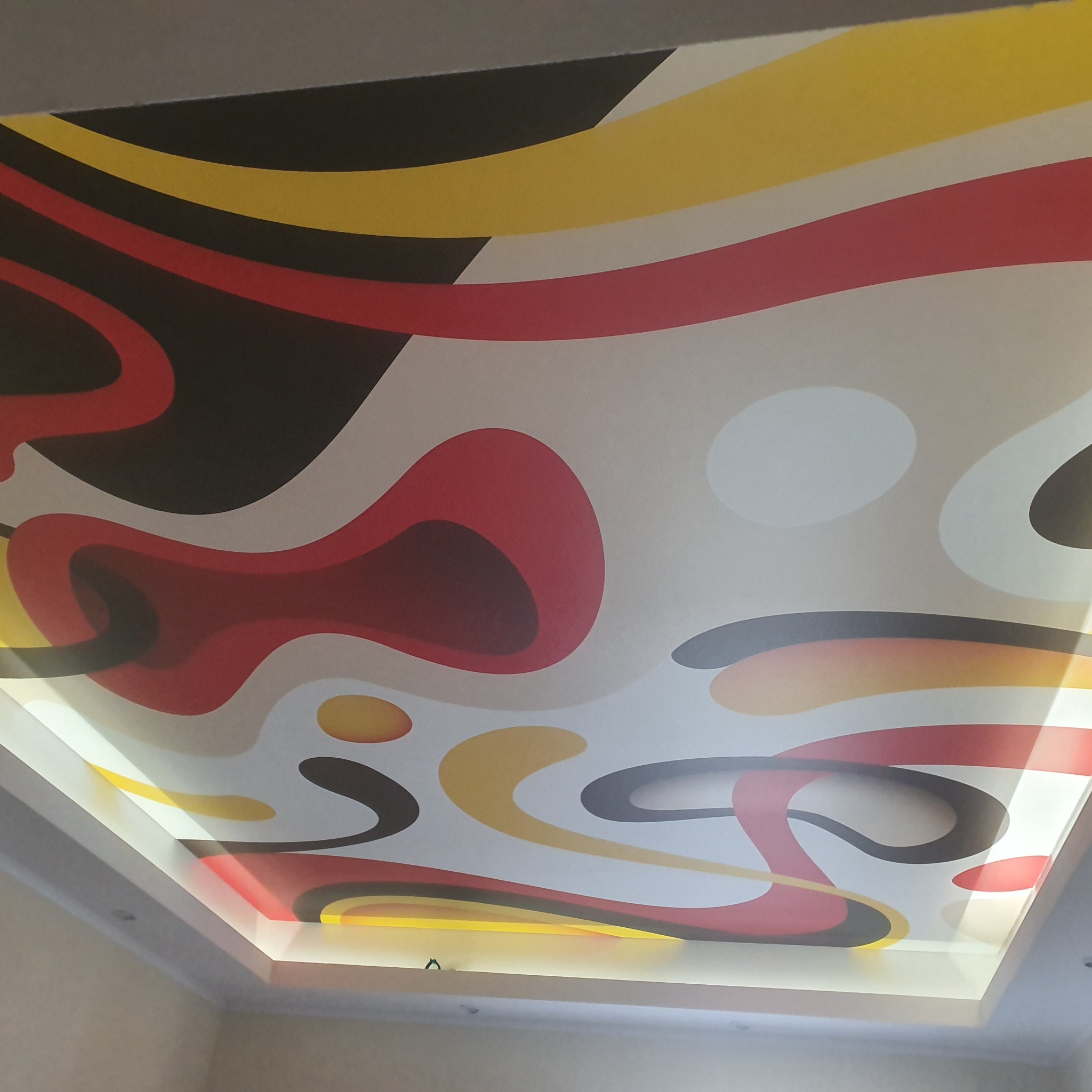 Abstrakcyjny wzór w kolorach czerwonym, żółtym i czarnym na podświetlanym suficie podwieszanym, widok z dołu.