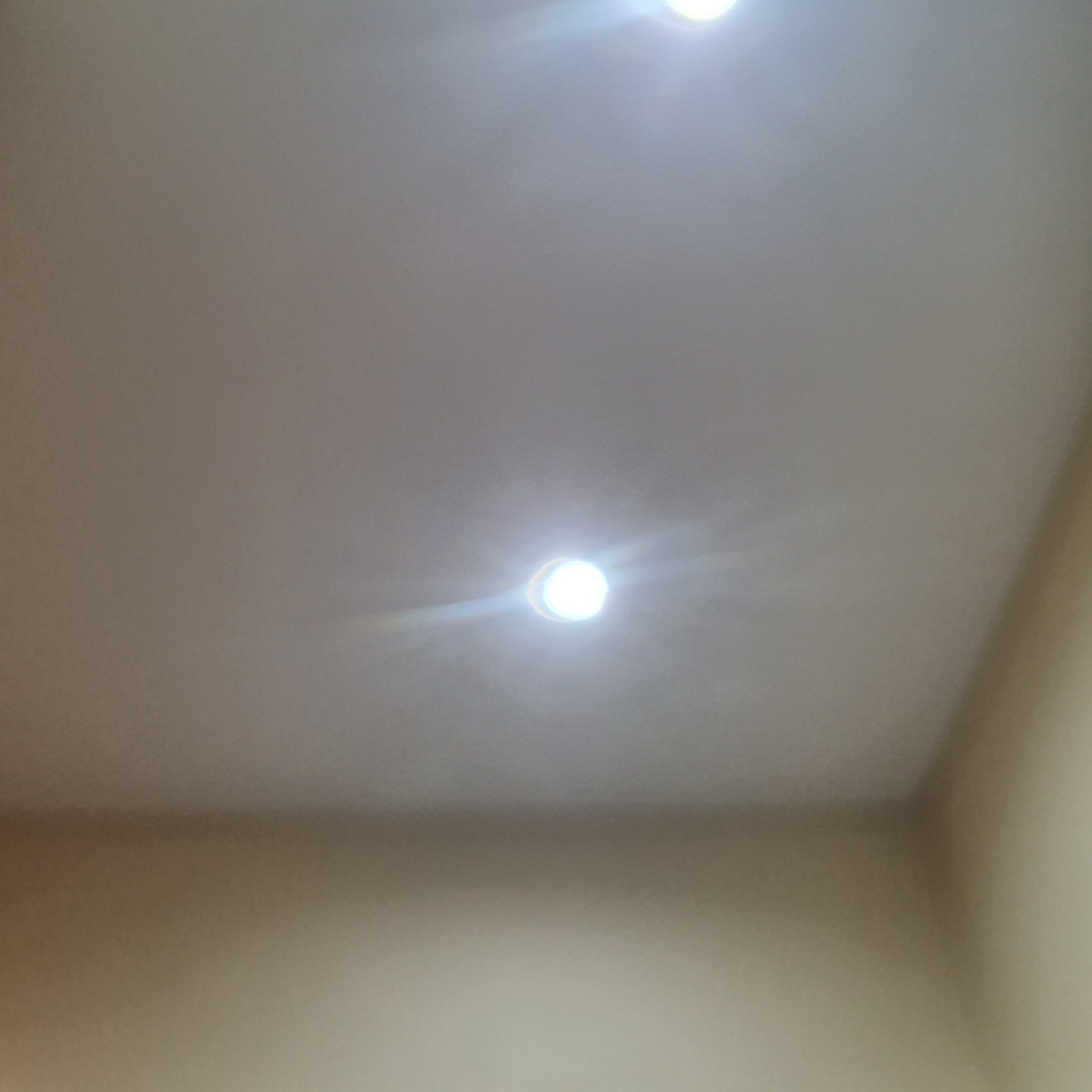 Biały sufit z trzema punktowymi lampami LED, sfotografowany pod kątem z bliska, oświetlając gładką powierzchnię.