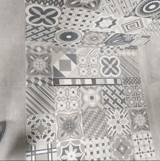 Wykończona łazienka z szaro-białymi, wzorzystymi płytkami na ścianie i podłodze, z odpływem liniowym w podłodze.