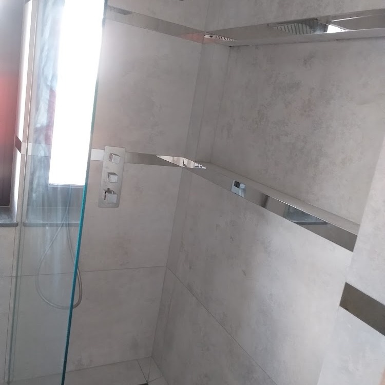 Wykończona łazienka z szarą, teksturowaną ścianą, kabiną prysznicową ze szklanymi drzwiami i chromowanymi listwami dekoracyjnymi oraz panelem sterowania prysznicem.