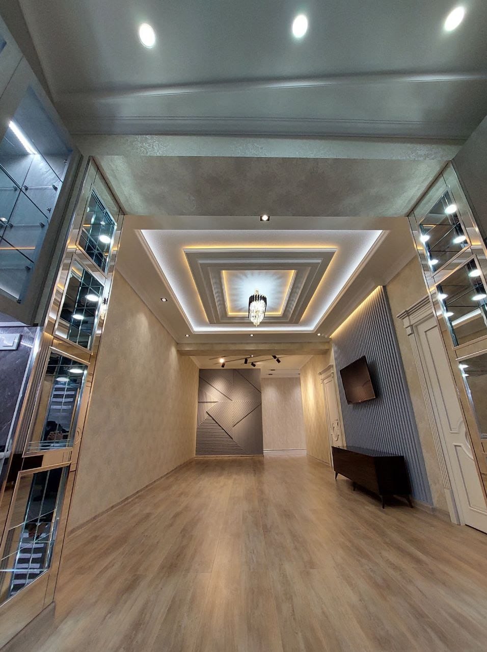 Nowoczesne wnętrze z podwieszanym sufitem z oświetleniem LED, lustrzanymi panelami na ścianach i drewnianą podłogą, minimalistyczna aranżacja ściany z geometrycznym wzorem.