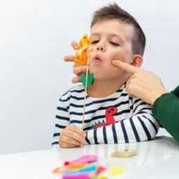 Chłopiec z dinozaurem na koszulce ćwiczy wymowę z pomocą terapeuty i pacynki w Trzebnicy.