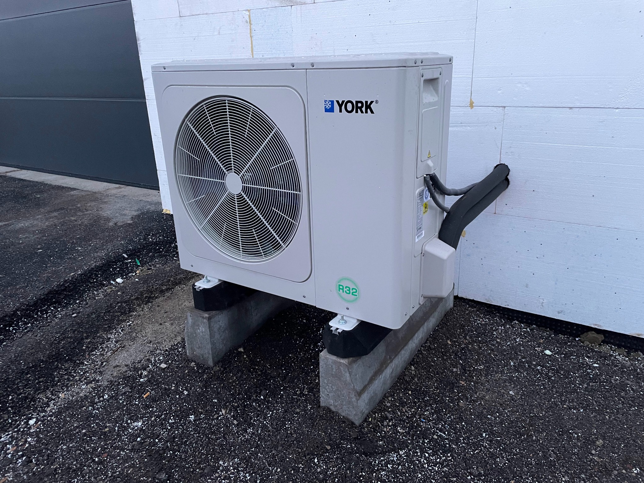 Zewnętrzna jednostka pompy ciepła marki York, zamontowana na betonowych podstawach przy ścianie budynku z widocznymi rurami instalacji.