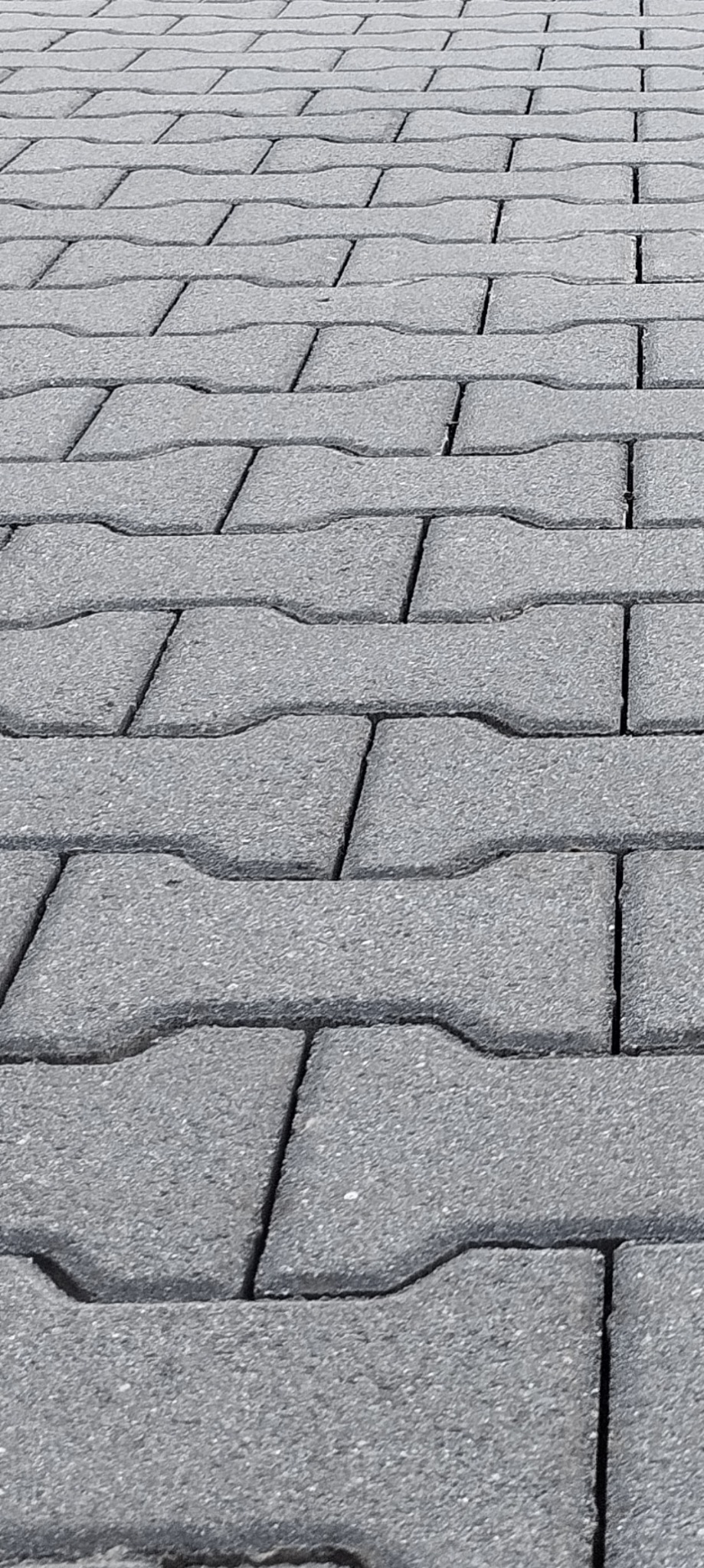Szara kostka brukowa ułożona w regularny wzór, widoczna z perspektywy lekko z góry, ukazująca teksturę i spoiny między elementami.