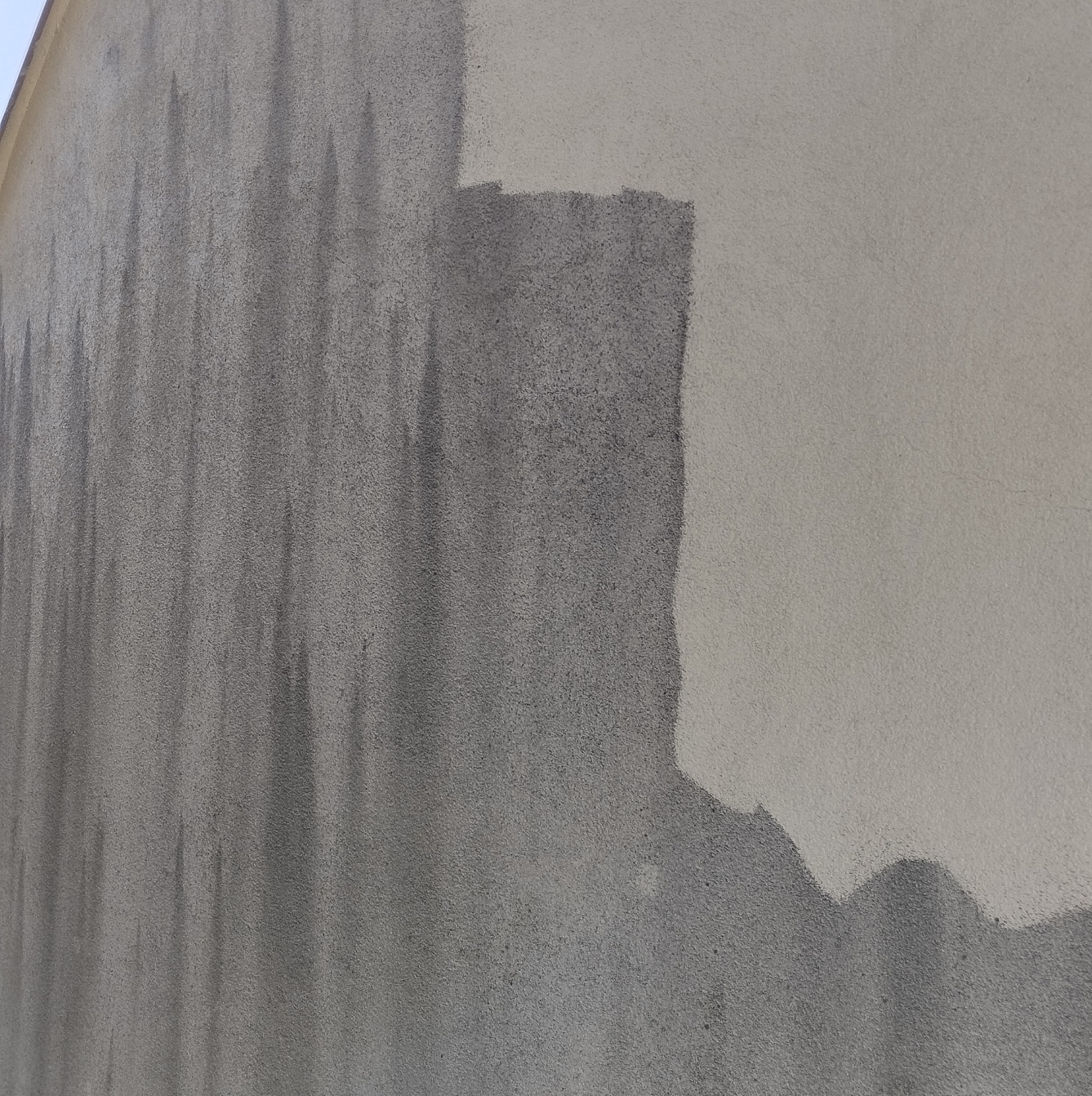 Fragment elewacji budynku z wyraźnym podziałem na obszar wyczyszczony i zabrudzony, ukazujący efekt przed i po. Widoczne pionowe smugi zabrudzeń na szarej, nieoczyszczonej części.