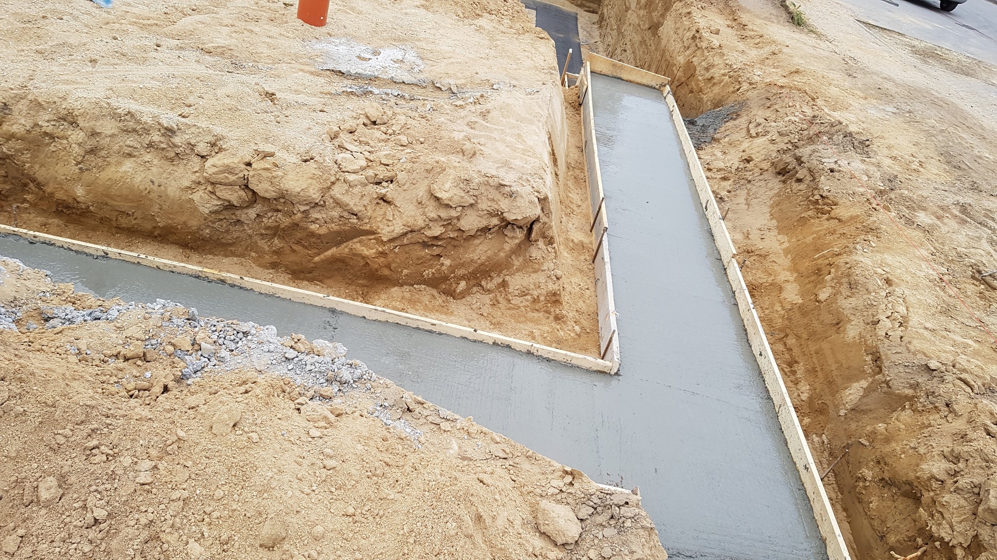 Wykop pod fundamenty zalany świeżym betonem, z widocznym drewnianym szalunkiem i ziemią wokół.