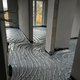 Białe rurki ogrzewania podłogowego ułożone na folii z nadrukiem w nowym budynku, widok z g&oacute;ry na instalację przed wylaniem posadzki.