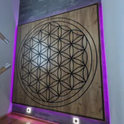 Drewniana ściana z wyciętym wzorem Kwiat Życia, podświetlona fioletowym światłem LED, widoczny fragment schodów z drewnianą balustradą.