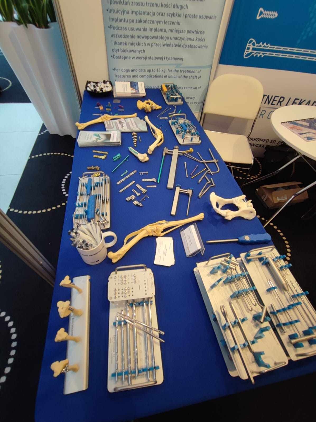 Ekspozycja narzędzi i modeli kości na niebieskim stole podczas targów medycznych w Dąbrowie Górniczej, prezentująca ofertę firmy z branży ortopedycznej.