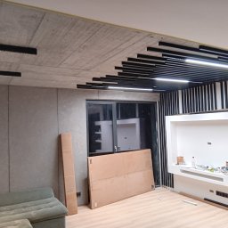 Lamele montowane do sufitu w różnych dlugosciach , sciana dekoracyjna efekt betonu oraz zabudowa poddaszy duzy telewizor wraz z półkami 