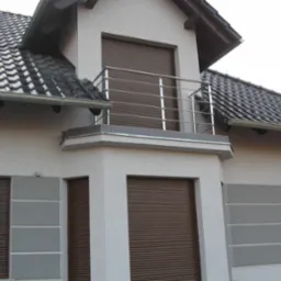 Balkon z nowoczesną, poziomą balustradą ze stali nierdzewnej, brązowe rolety zewnętrzne, elewacja w odcieniach szarości i bieli.