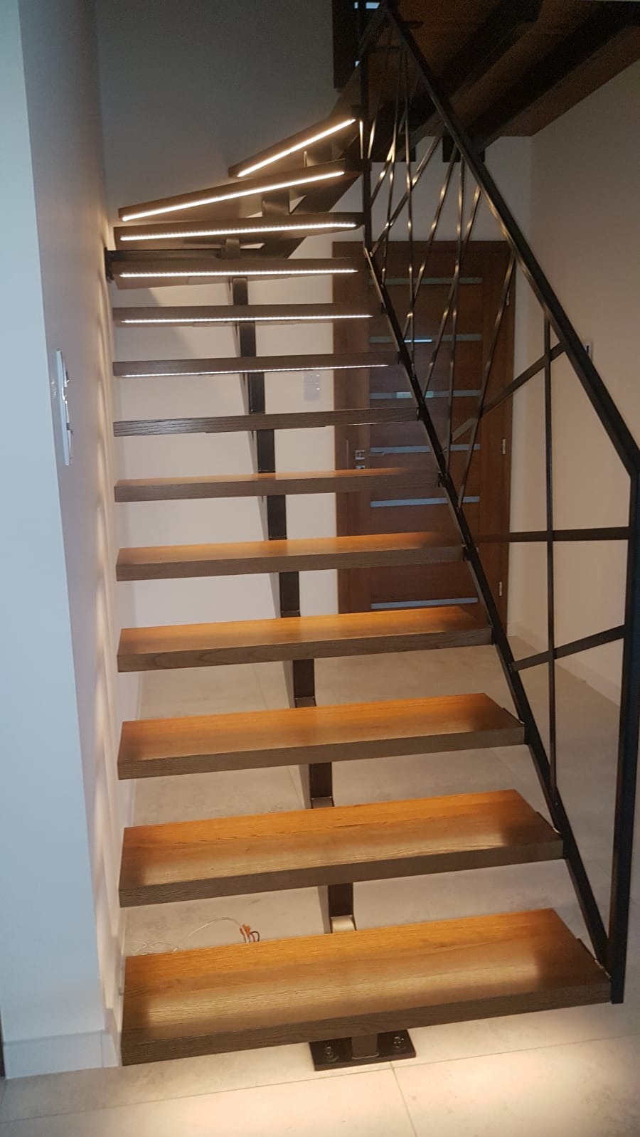Schody drewniane z metalową balustradą i podświetleniem LED zamontowanym pod każdym stopniem, widok z dołu.