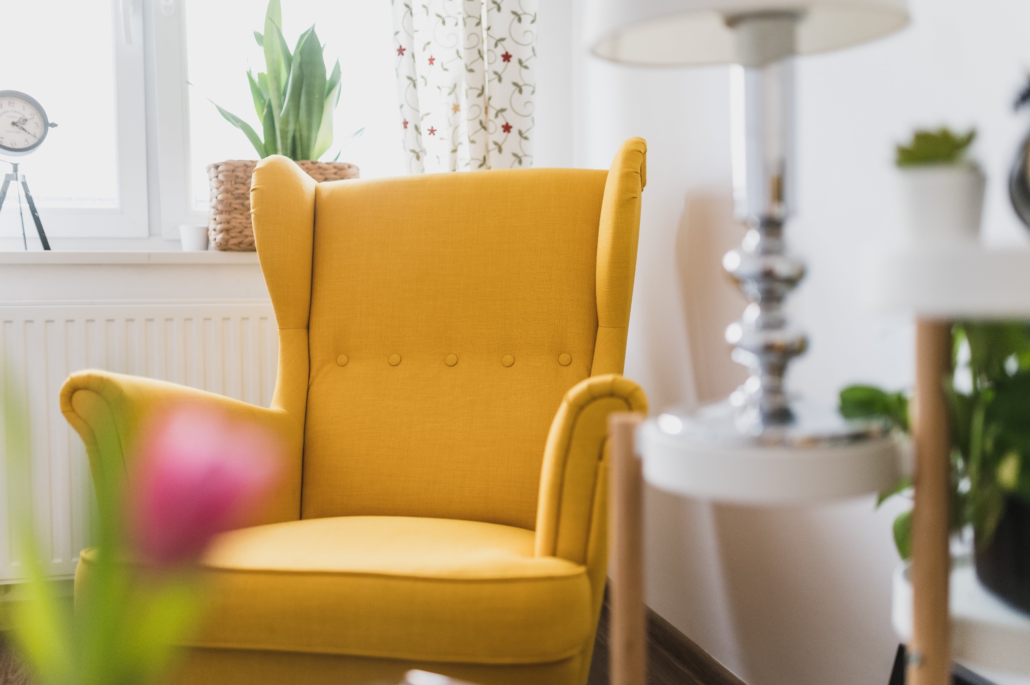Żółty fotel uszak w jasnym wnętrzu z roślinami doniczkowymi i lampą, widok z perspektywy niskiego kąta.