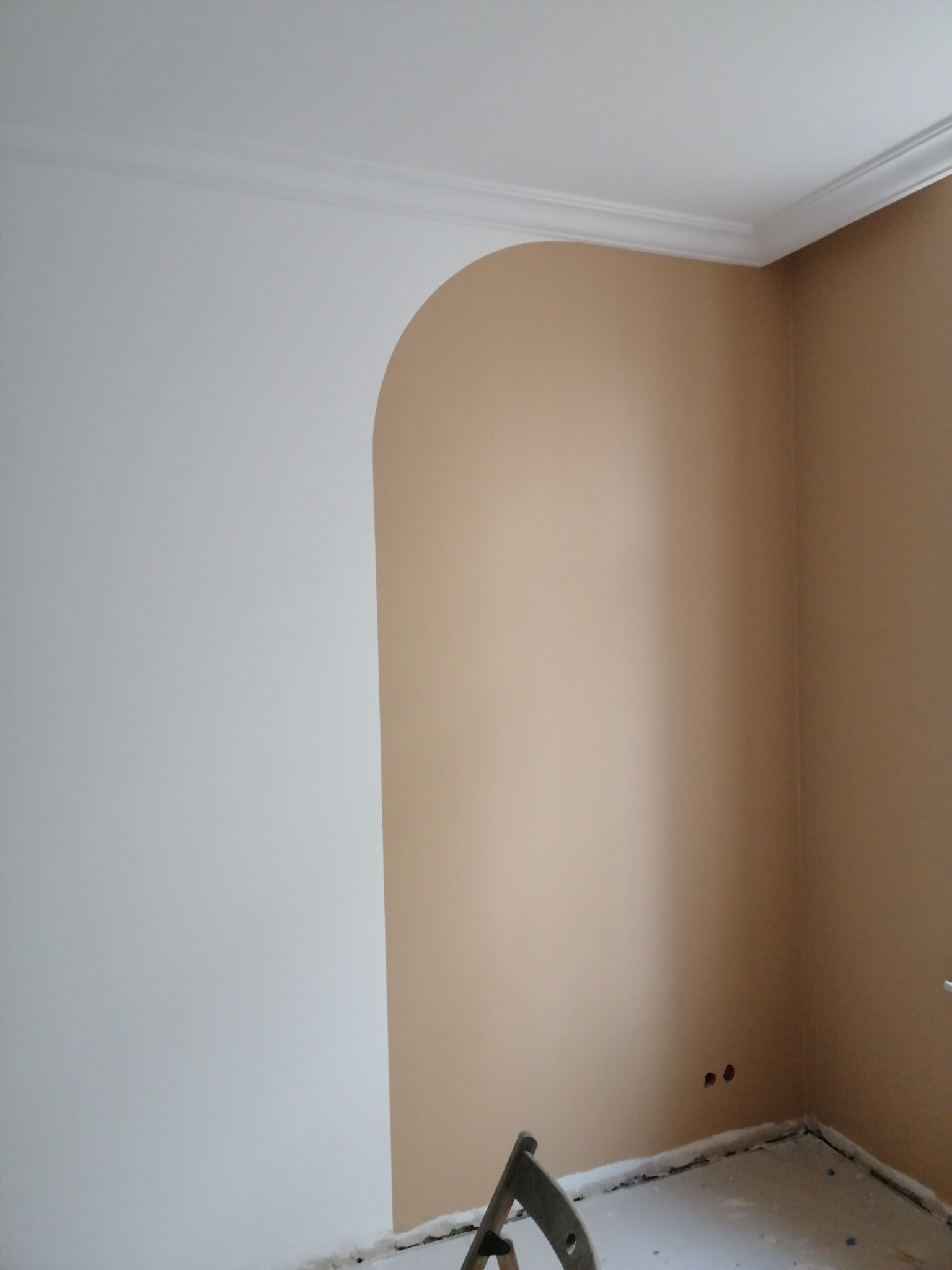 Ściana po malowaniu w Starogardzie Gdańskim, z fragmentem łuku pomalowanego na beżowo i białą listwą dekoracyjną pod sufitem, widoczne gniazdka elektryczne i zabezpieczona podłoga.