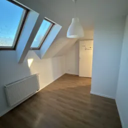 Poddasze po remoncie: drewnopodobne panele, białe ściany z grzejnikiem, okna dachowe i biała lampa wisząca, drzwi z napisem 'Princess'.