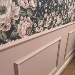 Ściana z dekoracyjnym, różowym panelem i tapetą w kwiaty, widok z boku.