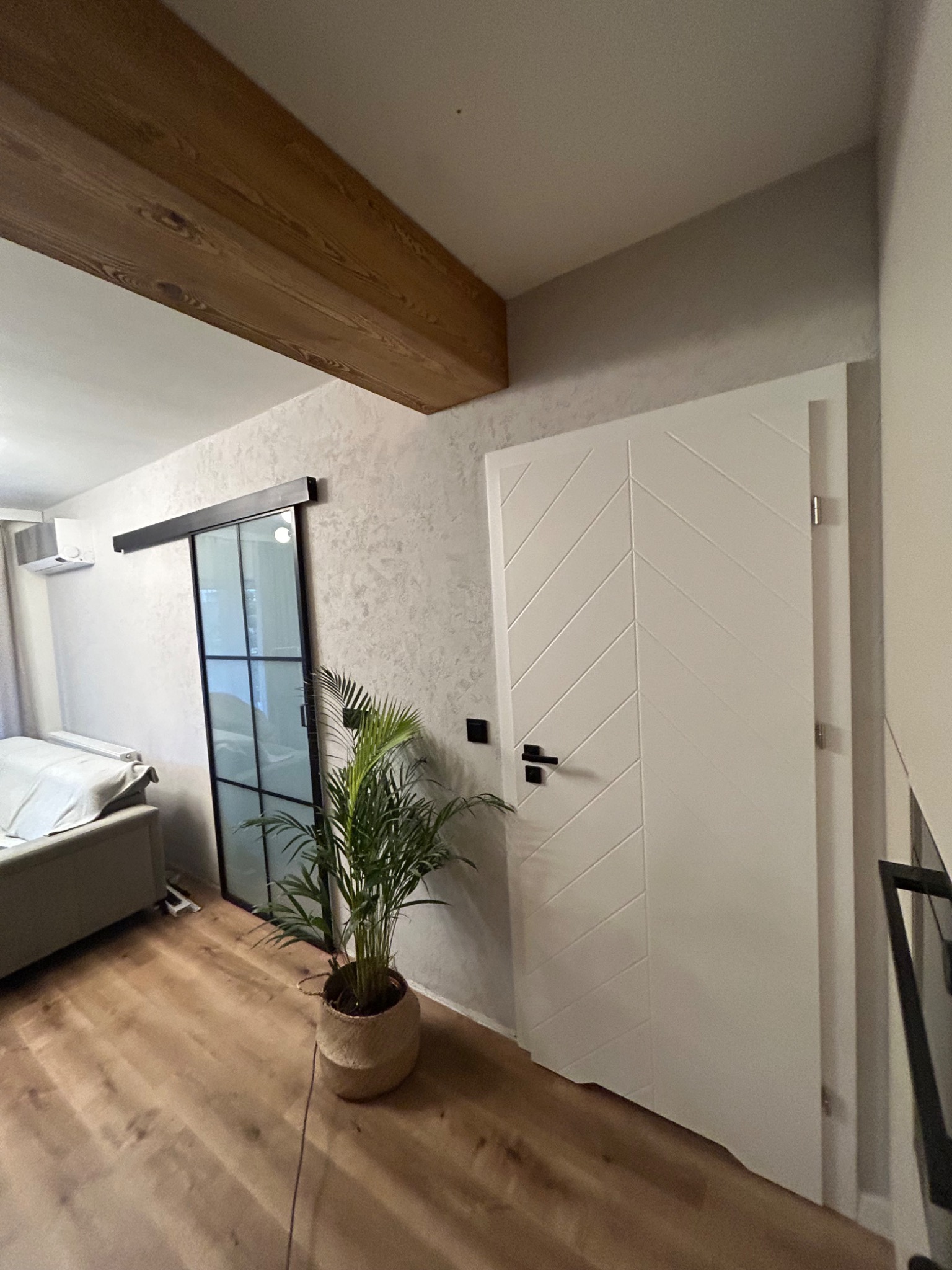 Nowoczesne wnętrze z drewnianą belką sufitową, przesuwnymi drzwiami loftowymi i białymi drzwiami z frezowanym wzorem w jodełkę. Parkiet na podłodze.