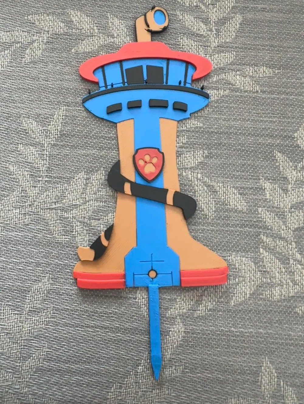 Kolorowa, wycięta laserowo dekoracja tortu w kształcie wieży z bajki Psi Patrol, wykonana w Somoninie, leży na szarym tle.