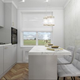 KC Office - Karolina Czyżewska - Jasna kuchnia z marmurowymi akcentami: białe szafki z złotymi uchwytami, marmurowy blat stołu z zastawą, dwa krzesła z szarym obiciem, parkiet w jodełkę, okno z widokiem na zielone pola.