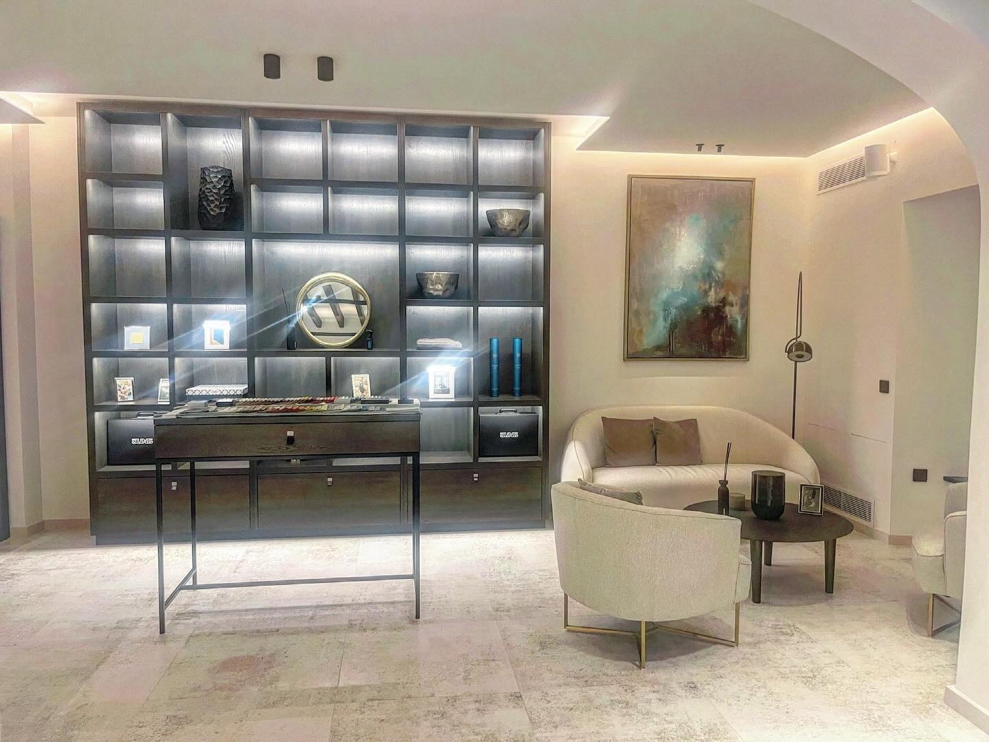 Jasne wnętrze z regałem podświetlanym LED, konsolą z próbkami kolorów, sofą i abstrakcyjnym obrazem.