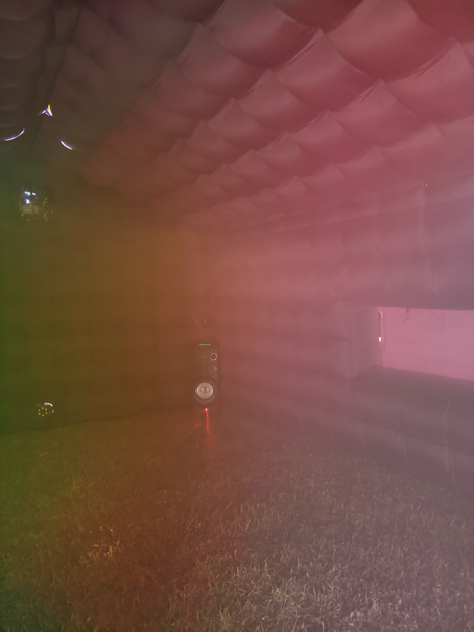 Wnętrze dmuchanej konstrukcji z podłogą z trawy, oświetlone kolorowymi światłami, w tle widoczny system nagłośnienia.