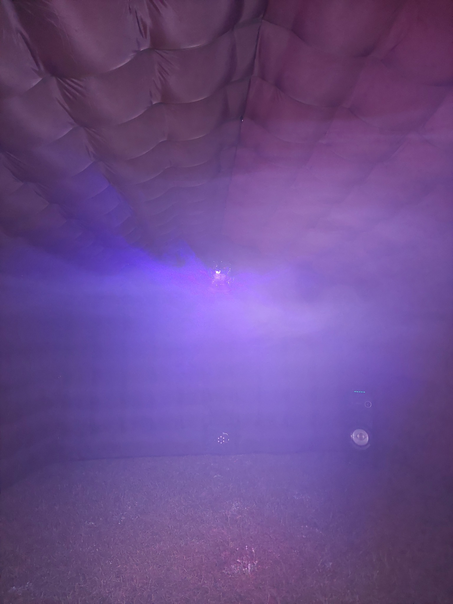 Wnętrze dmuchanej konstrukcji oświetlone fioletowym światłem, widoczna trawa na podłodze i charakterystyczna faktura ścian.