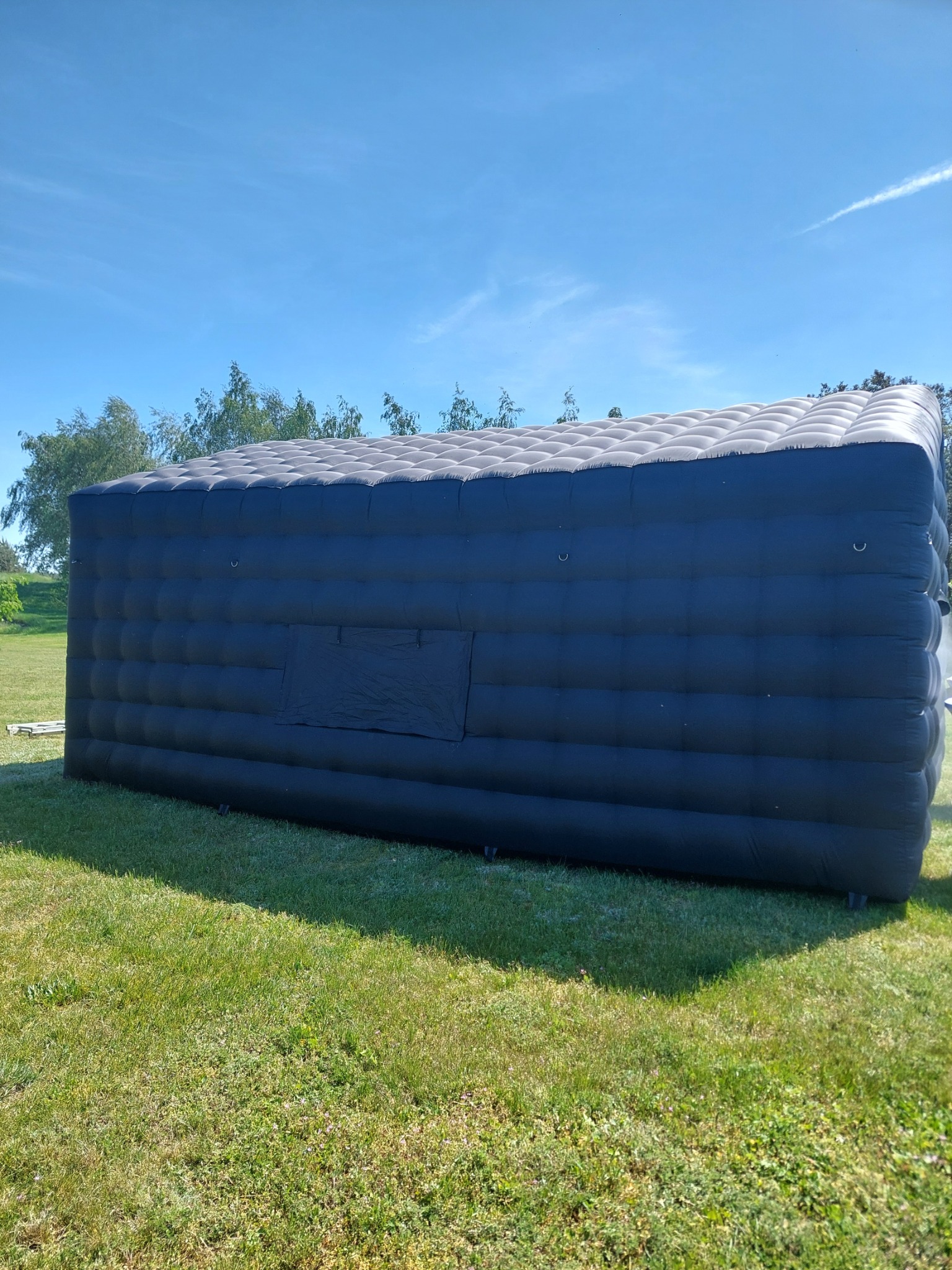 Czarny dmuchany namiot kubaturowy z widocznym oknem wentylacyjnym, ustawiony na trawie w plenerze przy słonecznej pogodzie.