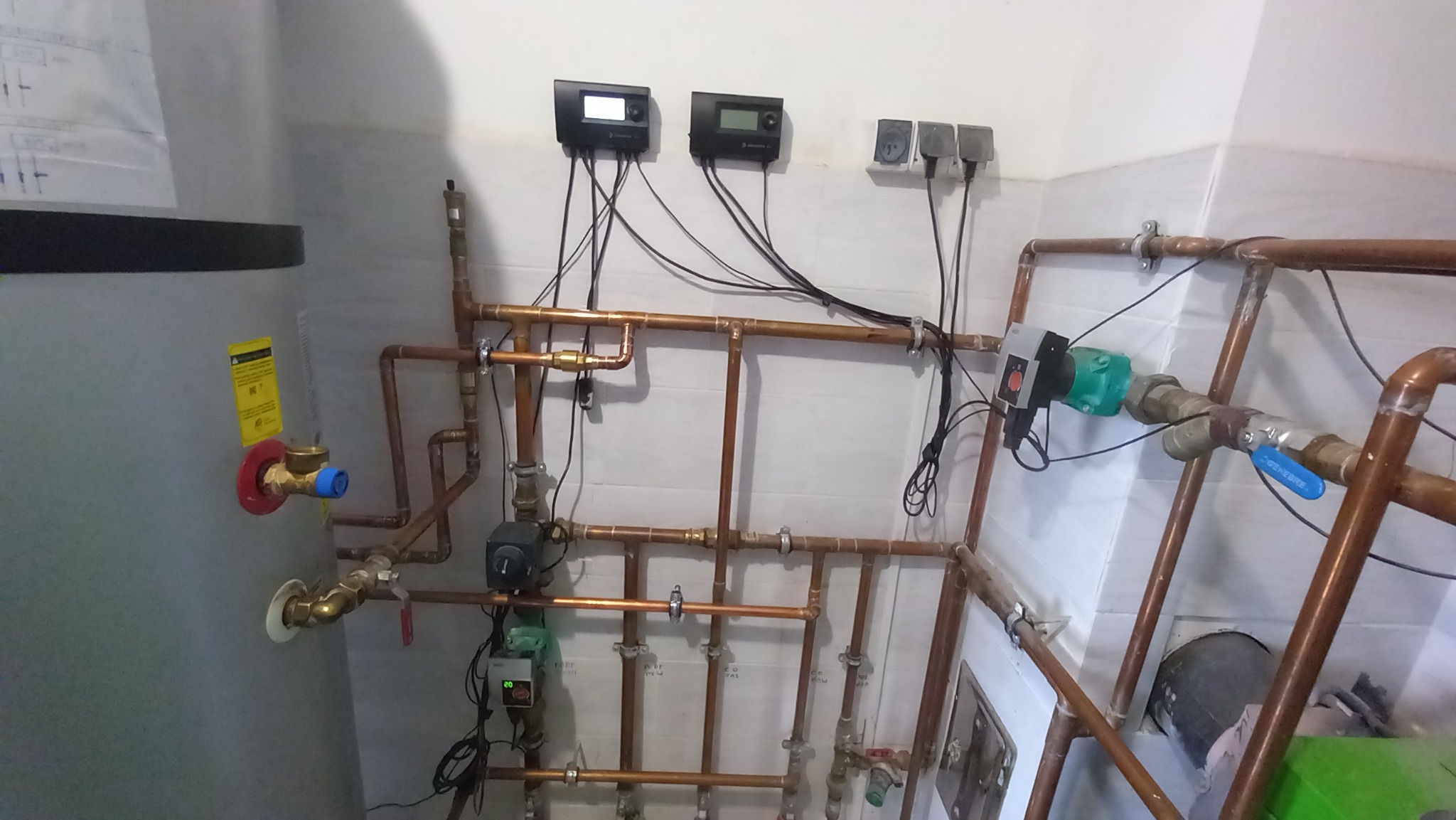 Kompleksowy system rur miedzianych, zaworów i sterowników elektronicznych zamontowany na białej ścianie z płytek, element instalacji centralnego ogrzewania.