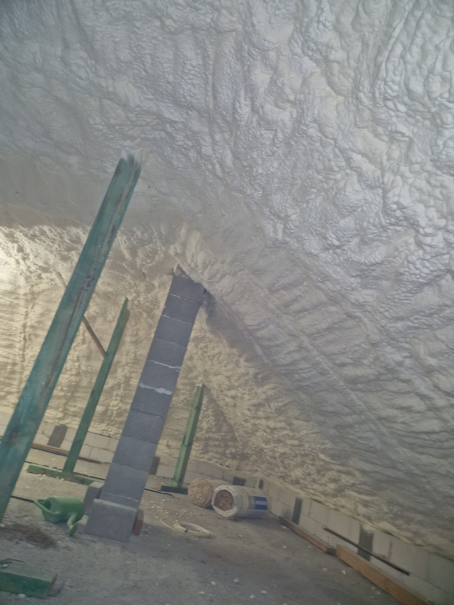 Poddasze po aplikacji szarej pianki izolacyjnej, widoczne drewniane elementy konstrukcyjne, bloczki betonowe i zielona konewka