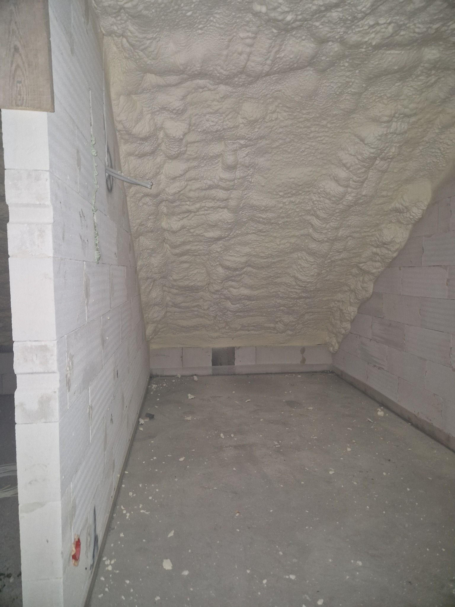 Poddasze z izolacją pianką PUR, widoczne ściany z bloczków betonowych i przewody elektryczne.