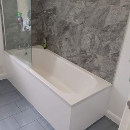 Prywatny wykonawca - Wykończona łazienka w Przemyślu: biała wanna z parawanem nawannowym, szare płytki imitujące marmur na ścianie i podłodze.