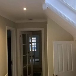 Prywatny wykonawca - Korytarz po malowaniu w odcieniach beżu i bieli z widocznymi schodami, drzwiami i oświetleniem punktowym.