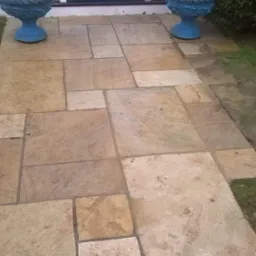 Ułożona z nieregularnych płyt ścieżka z piaskowca prowadząca do błękitnych drzwi wejściowych, po bokach ozdobne, błękitne donice z zielonymi roślinami.