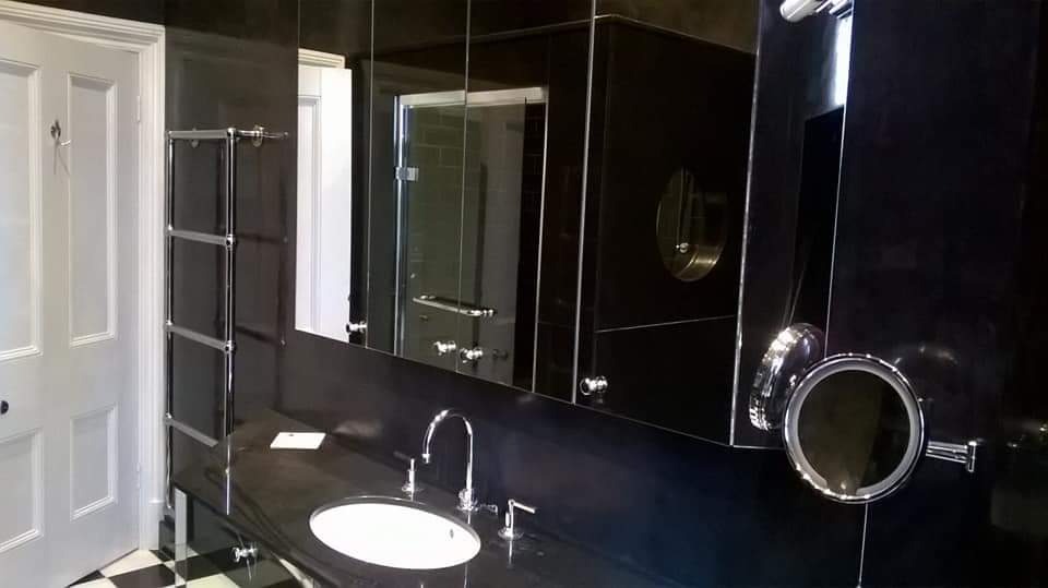 Nowoczesna łazienka w czerni z białymi akcentami, armatura chromowana, podłoga w szachownicę, widoczna kabina prysznicowa w tle.