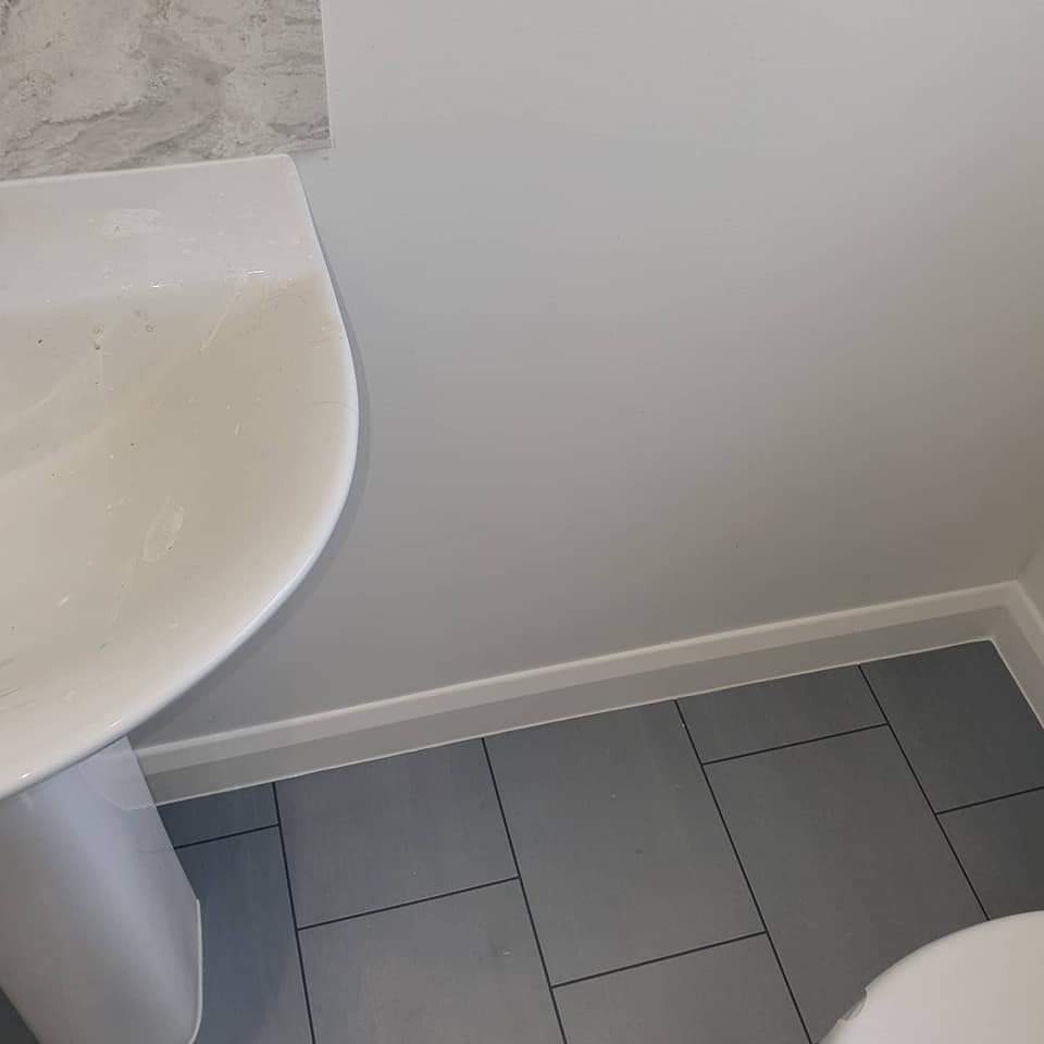 Fragment łazienki po remoncie: umywalka na postumencie, szare płytki podłogowe i białe ściany z marmurowym akcentem u góry.