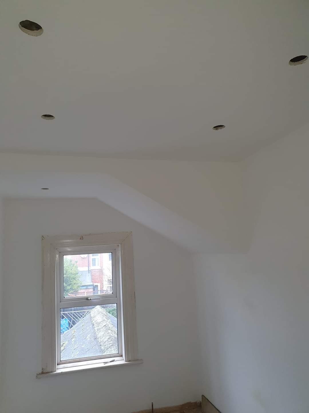 Białe ściany i sufit w pokoju po malowaniu, z oknem i otworami pod oświetlenie w suficie.