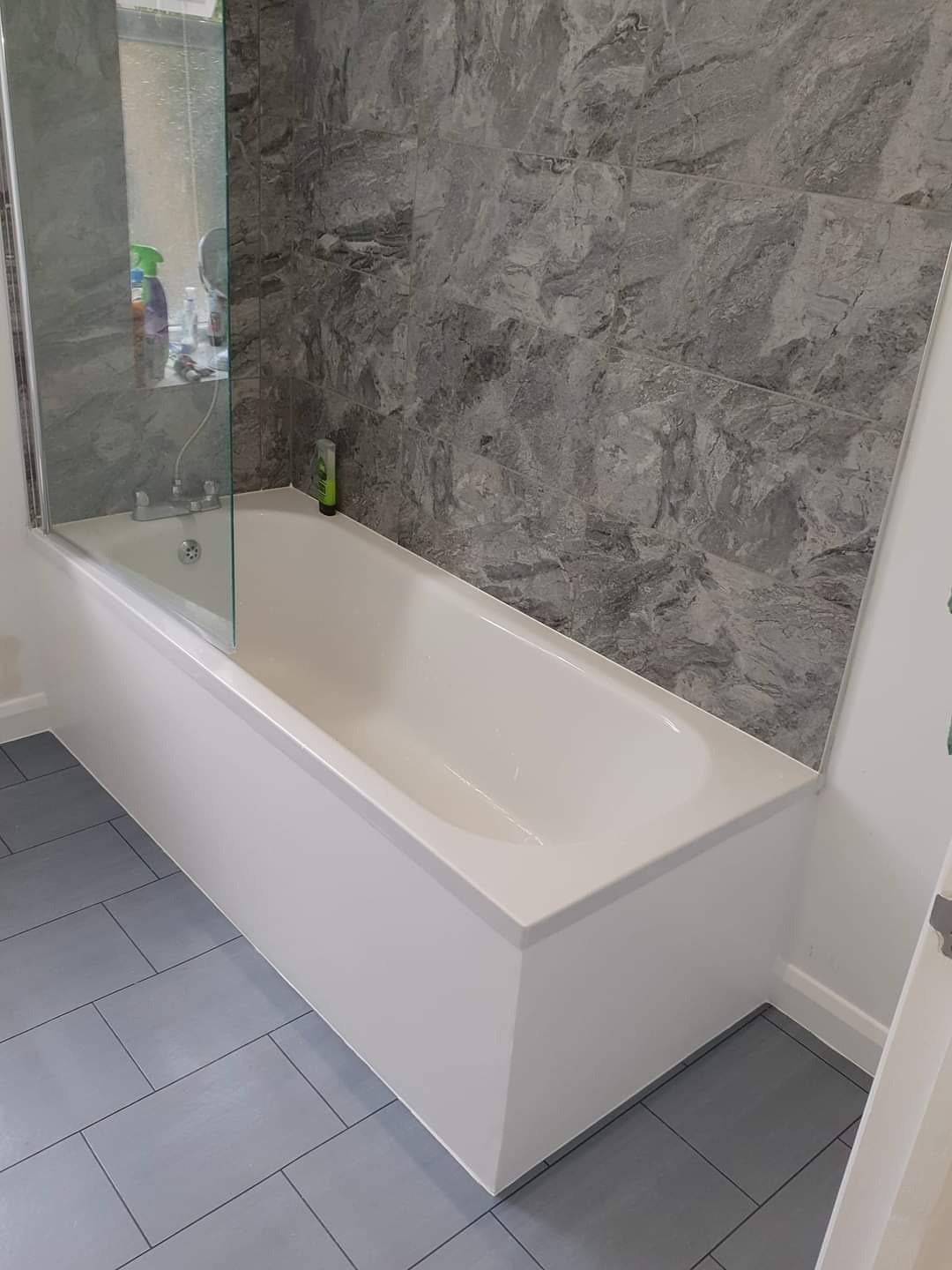 Wykończona łazienka w Przemyślu: biała wanna z parawanem nawannowym, szare płytki imitujące marmur na ścianie i podłodze.