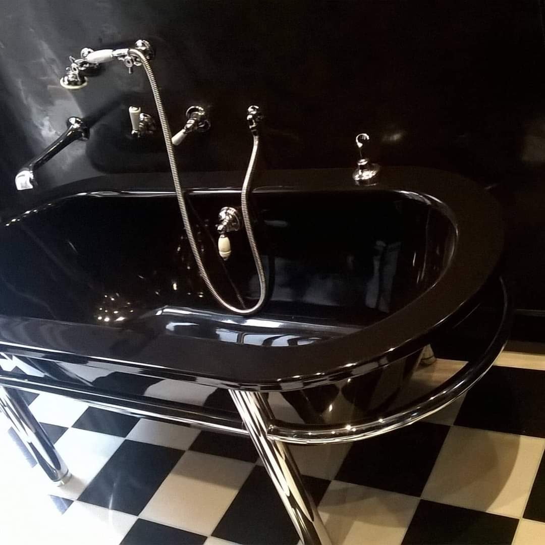Czarna, wolnostojąca wanna na chromowanych nóżkach, z armaturą w stylu retro i szachownicową podłogą w tle.