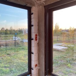 Elektro Świat Oleksandr Pashutkin - Surowy stan: białe kable i pomarańczowe puszki elektryczne na ścianie z betonu komórkowego, widoczne przez okno w nowym budynku w trakcie budowy.