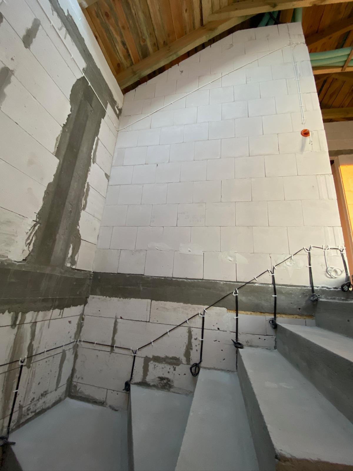 Surowe wnętrze w trakcie prac wykończeniowych: ściany z betonu komórkowego, widoczne przewody elektryczne prowadzone po ścianach, drewniany strop.