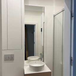 CUADRO PLUS Mariia Alfimova - Nowoczesna łazienka z białą umywalką nablatową, szafką z lamelami, kabiną prysznicową i zabudową meblową pod sufit, odbicie lustrzane wnętrza z kartonami.