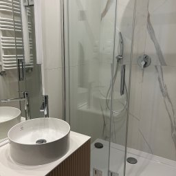 CUADRO PLUS Mariia Alfimova - Nowoczesna łazienka z kabiną prysznicową ze szklanymi drzwiami, umywalką nablatową marki Laufen na szafce z ryflowanym frontem oraz grzejnikiem drabinkowym w tle.