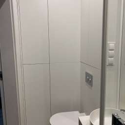 CUADRO PLUS Mariia Alfimova - Nowoczesna, minimalistyczna łazienka z białymi szafkami w zabudowie, podwieszaną miską WC i okrągłą umywalką nablatową na szafce z lamelami, marmurowa podłoga.