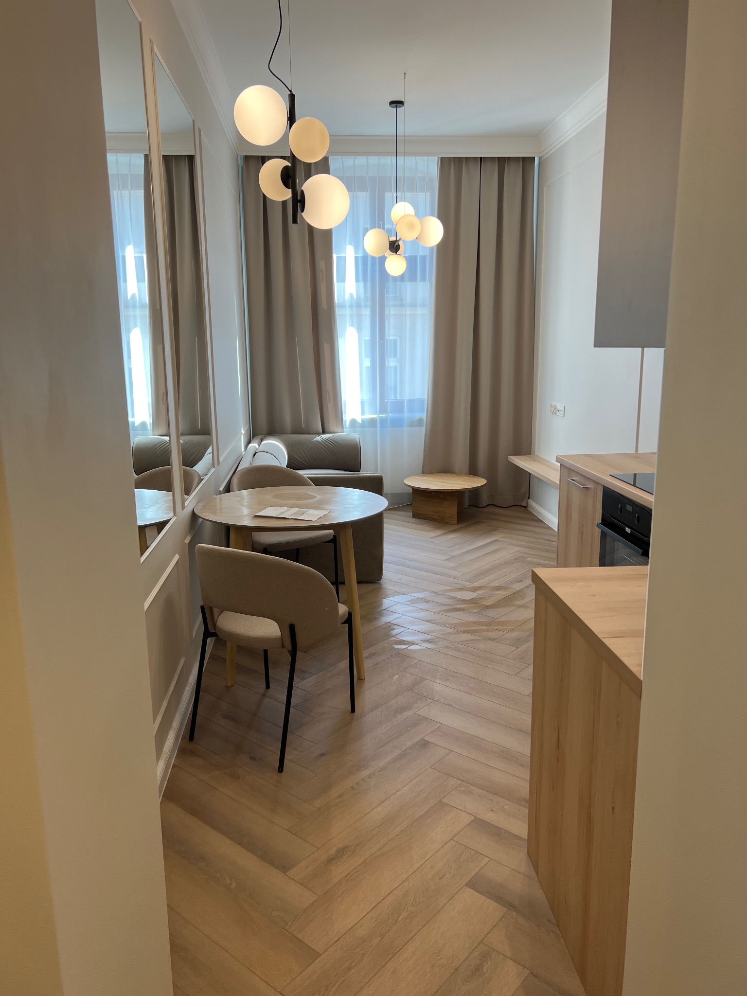 Jasne wnętrze mieszkania z parkietem w jodełkę, okrągłym stołem z krzesłami i nowoczesnym oświetleniem kulistym.