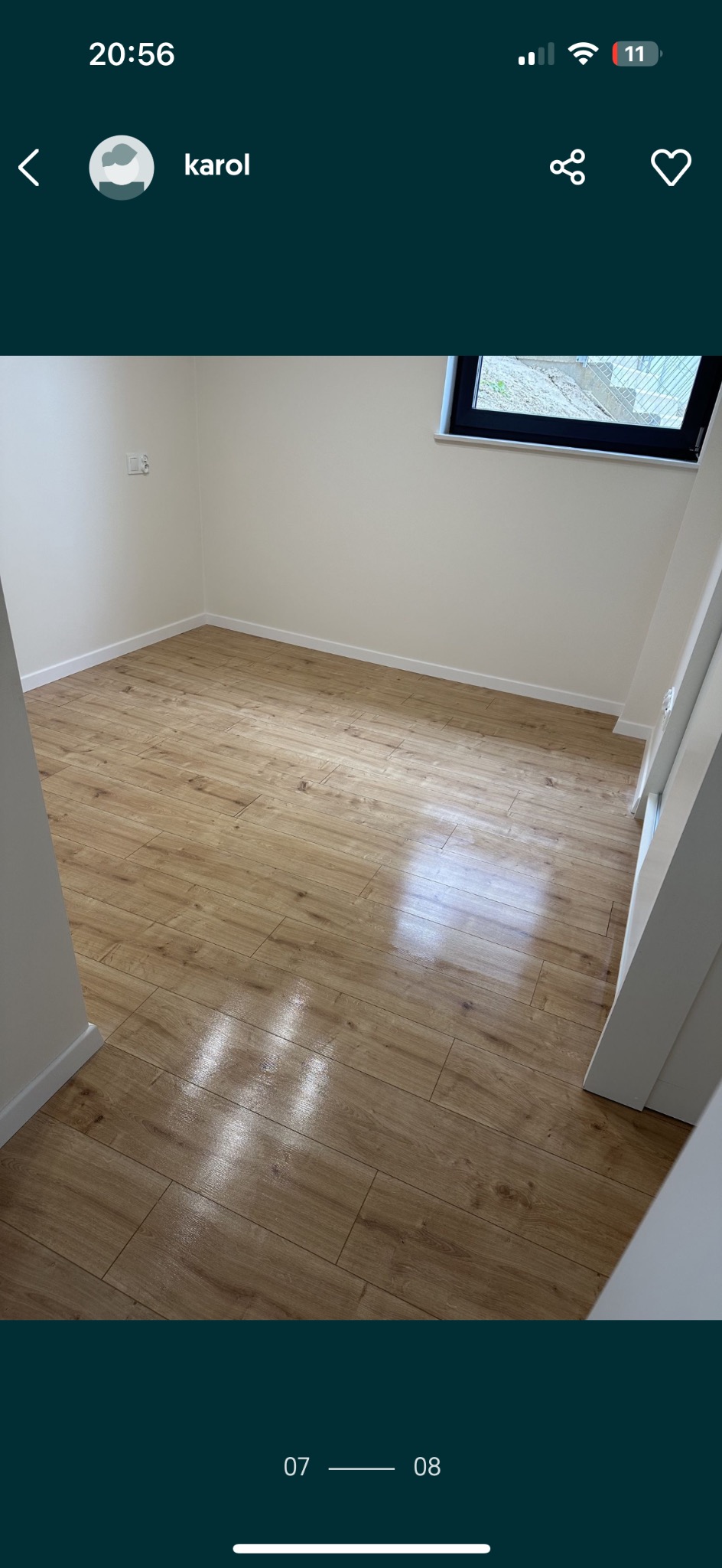 Nowo położona podłoga z paneli imitujących drewno, widoczne jasne ściany i okno z widokiem na zewnątrz.