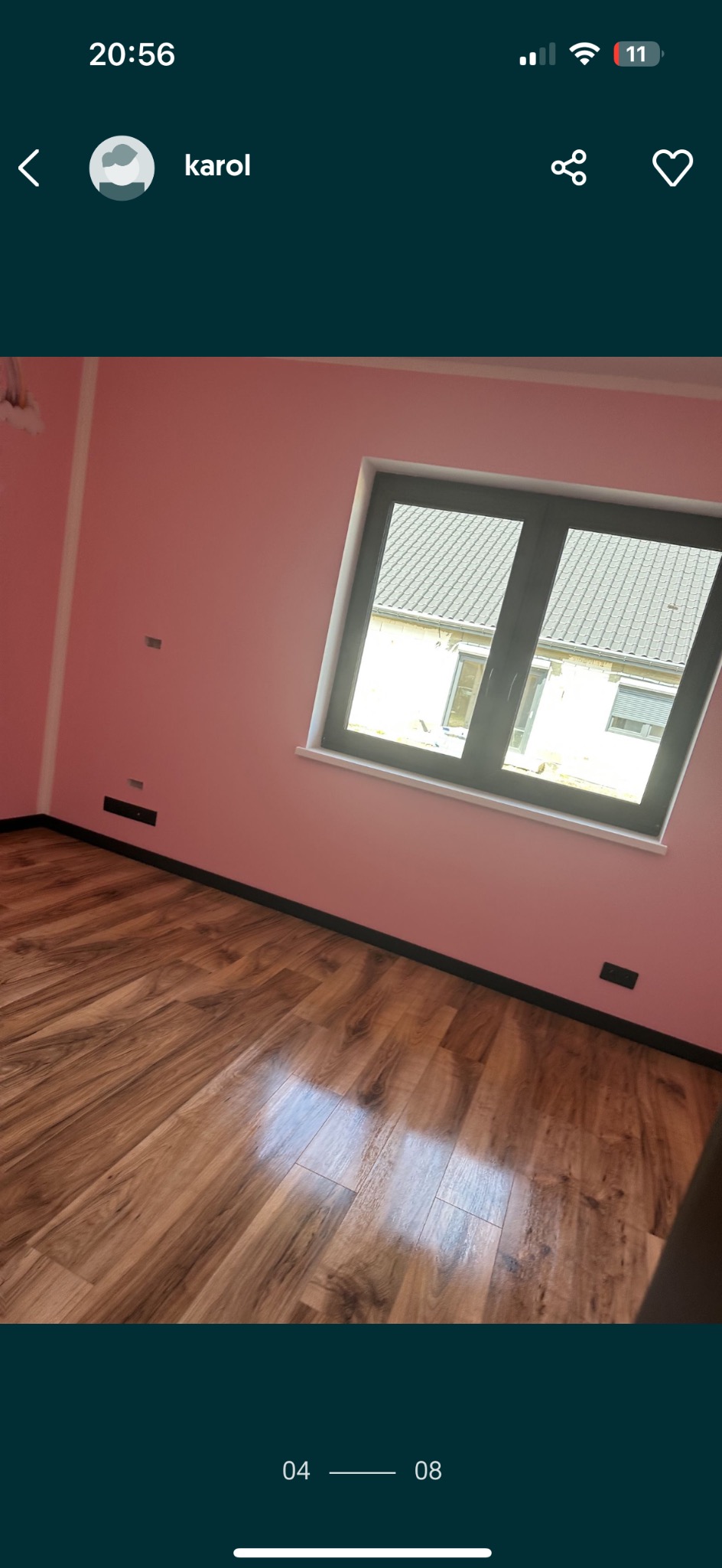 Świeżo wykończone wnętrze z panelami podłogowymi w odcieniach brązu, różowymi ścianami i ciemnoszarym oknem, widok z niskiej perspektywy.