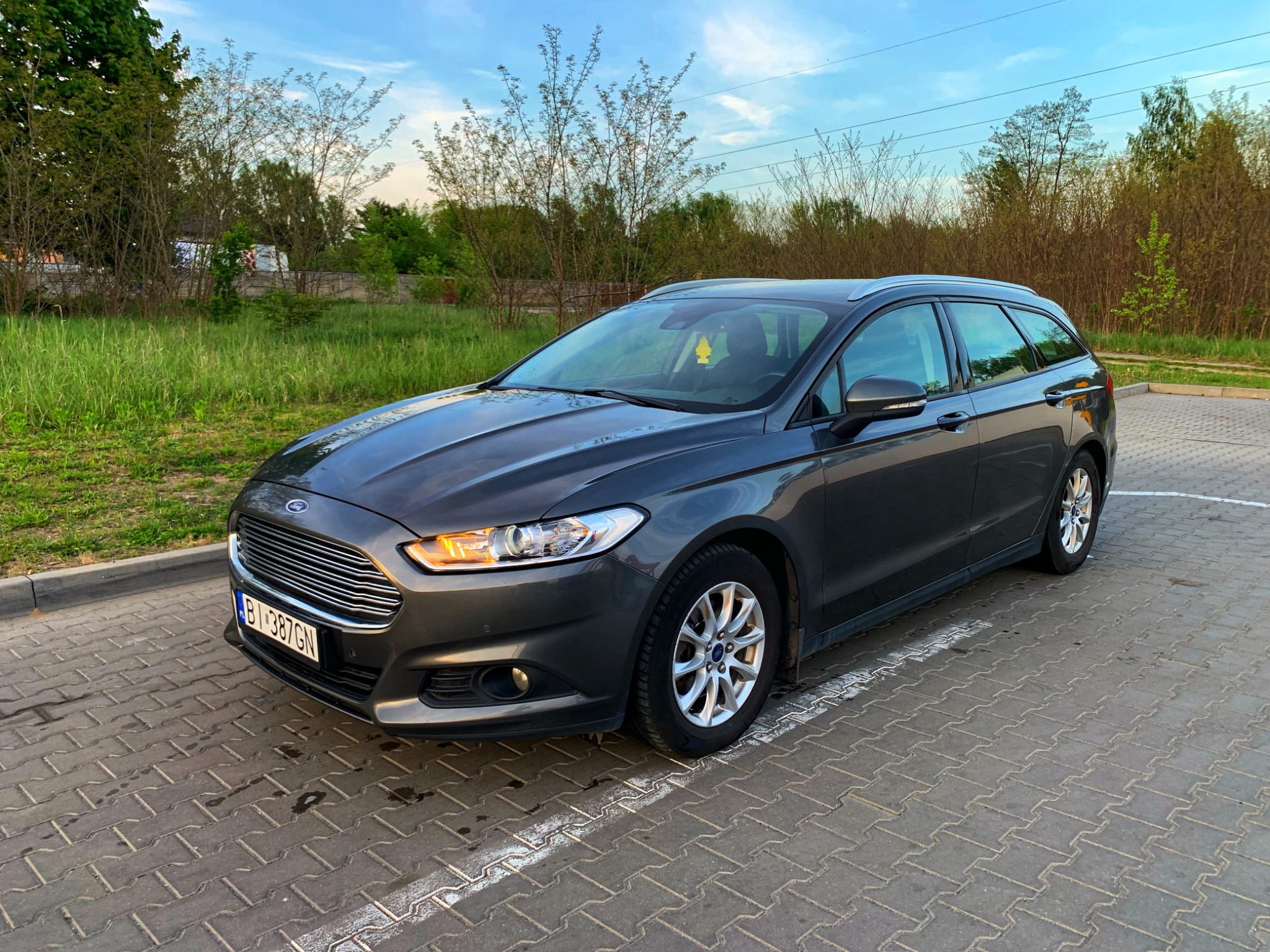 Szary samochód kombi Ford Mondeo zaparkowany na kostce brukowej, widoczny z przodu pod kątem, z numerem rejestracyjnym B1 387GN.