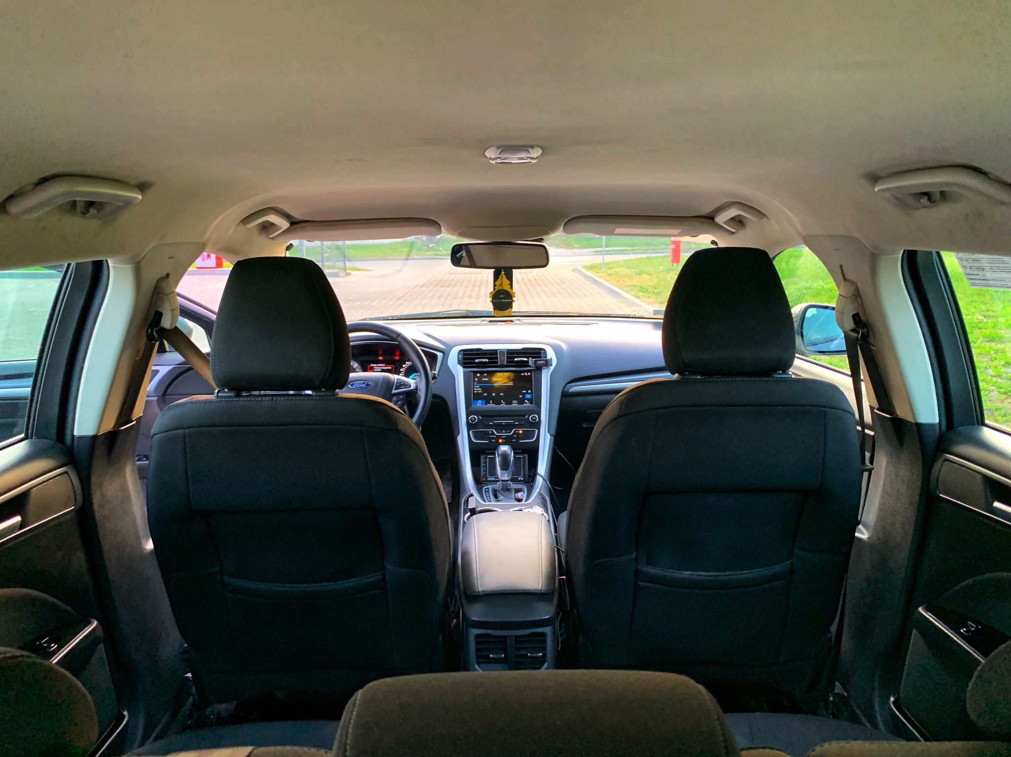 Wnętrze samochodu Ford Fusion widziane z tylnej kanapy, z widoczną deską rozdzielczą, konsolą środkową i zagłówkami przednich foteli.